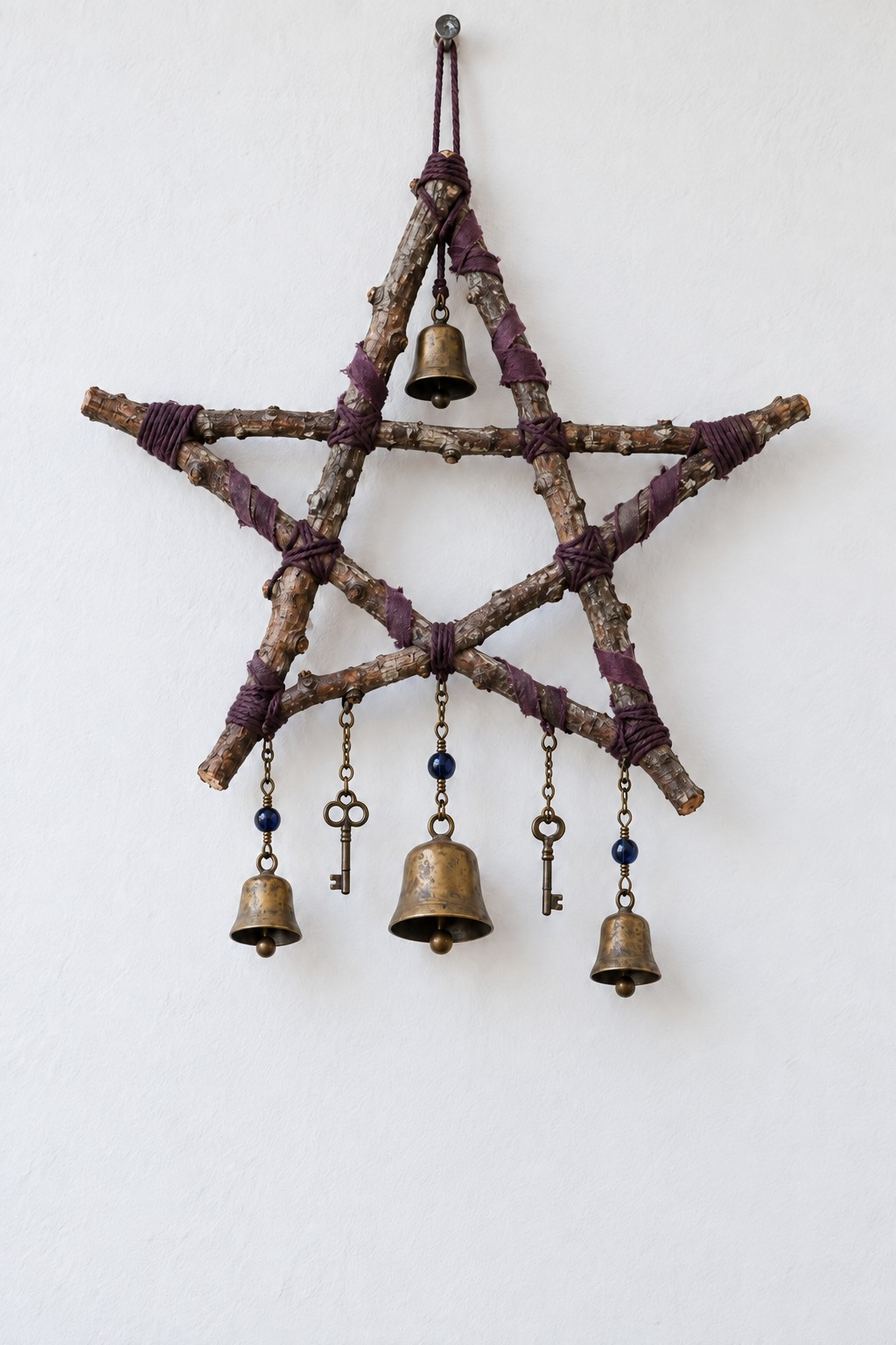 Twig pentagram bound with plum fabric, one bell inside the top point and three bells and two keys hanging below
